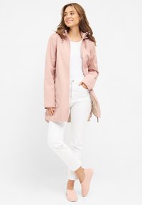 Jasnoróżowa wodoodporna kurtka z zamkiem z przodu, kieszeniami bocznymi i regulowanym kapturem, zestawiona z białymi spodniami i jasnoróżowymi butami wsuwanymi.