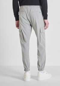 Achteraanzicht van een persoon in lichtgrijze cargobroek met elastische boorden, witte sneakers en een zwart langemouwen top tegen een effen achtergrond.