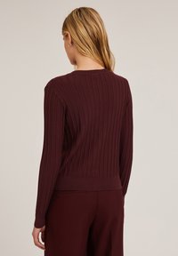 Bordowy sweter prążkowany z okrągłym dekoltem i długimi rękawami, z dopasowanym wykończeniem i gładką fakturą. Bez widocznych wzorów ani akcentów.