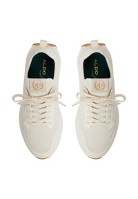 Zapatillas deportivas blancas con parte superior de malla, puntera redonda y cordones planos. Cuenta con una suela en tono marrón y acentos dorados en la lengüeta y la plantilla.