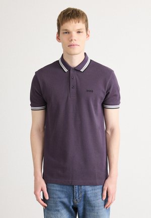 Lilla polo-skjorte med klassisk krage, tre knapper og stripete mansjetter. "BOSS"-logoen er vist på venstre bryst. Kombinert med blå jeans.