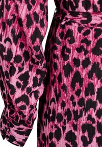 Roza in črna obleka s leo printom, dolgimi napihnjenimi rukavi, poudarjenim pasom in teksturiranimi detajli. Ima gumbne manšete.