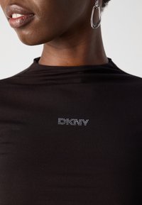 Black fitted t-shirt with a high neckline, featuring the brand name "DKNY" in metallic rhinestones on the front. Soft, stretchy fabric.