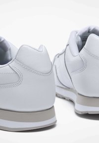 Weiße Sneakers mit einem glatten Lederobermaterial, runder Zehenform und einer strukturierten Gummisohle mit einem hellgrauen Akzent in der Nähe der Ferse.