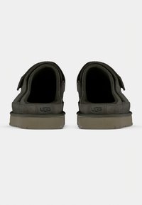 Chaussures UGG grises avec une extérieure en suède doux, une semelle en caoutchouc plate, et une simple bride Velcro sur chaque chaussure pour un enfilage facile.