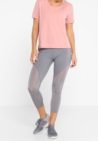 Rosa V-Ausschnitt T-Shirt und graue Caprihosen mit Netzpaneelen, die eine glatte Textur und eine sportliche Passform aufweisen, kombiniert mit grauen Turnschuhen.