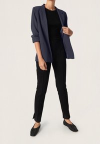 Blazer azul marino con mangas remangadas, top negro ajustado, pantalones negros entallados y zapatos planos negros con textura fruncida. Diseño simple y a medida.