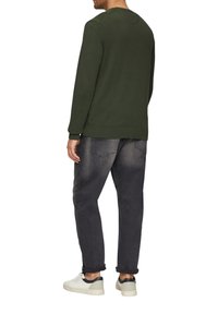 Grüner Pullover mit rundem Halsausschnitt, gerippten Bündchen und Saum, kombiniert mit dunkelgrauen Jeans und weißen Sneakers. Von hinten betrachtet.