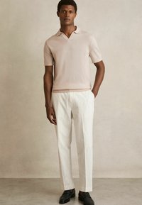 Ljusrosa kortärmad polo, vitrandiga skräddarsydda byxor, svarta loafers, mjuk textur, figursydd design, minimalistisk stil.