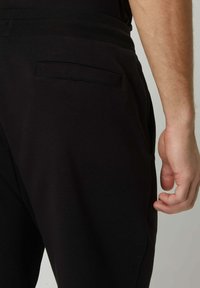 Pantalon de jogging noir en tissu doux, avec une poche latérale et une taille élastique pour le confort. La texture semble lisse.
