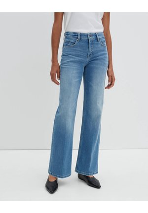 Jean large bleu clair en denim, avec un délavage, cinq poches et passants de ceinture, associés à des chaussures noires à talons pointus.