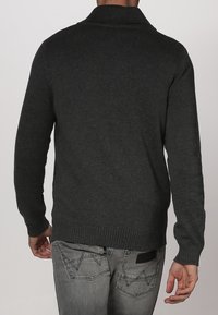 Mörkgrått stickad kardigan med sjalkrage, har ribbade ärmslut och fåll. Bärs över urtvättade jeans med distinkt sömnad.