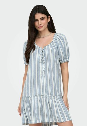 Młoda kobieta z długimi ciemnymi włosami, ubrana w białą sukienkę w pionowe niebieskie paski, z krótkimi bufkami i wiązaniem z przodu.