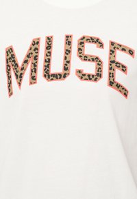 Λευκό βαμβακερό t-shirt με την επιγραφή "MUSE" σε έντονα γράμματα. Το κείμενο έχει σχέδιο λεοπάρδαλης με πορτοκαλί περίγραμμα για αντίθεση.