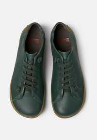 Green leather sneakers with a rounded toe, elastic laces, and a textured sole. Includes brown accents and a printed brand logo inside.