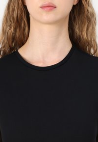 Svart kortermet topp med rund hals laget av glat stoff, med et tettsittende design og en ren, minimalistisk halslinje.