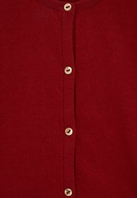 Lähikuva punaisesta neulotusta kankaasta, jossa on pystysuora rivi neljästä vaaleanvärisestä napista.