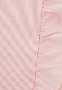 Rosa tyg med vertikal ribbning, med en rynkad kant i samma nyans. Mjuk textur med en svag lyster, slät nära volangen.