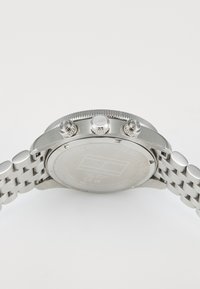 Orologio in acciaio inossidabile argentato con una lunetta testurizzata, tre pulsanti e un bracciale a maglie metalliche. Presenta un fondello inciso, liscio.