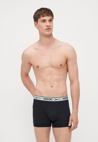 Black cotton boxer briefs with a patterned green and black waistband featuring the Nike logo, fitted design with a soft texture.