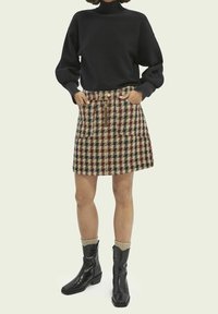 Sort sweatshirt med lange ærmer, ternet mini skirt i beige, brune og blå nuancer, med lynlås foran og to lommer, parret med sorte ankelstøvler.