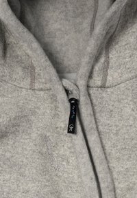 Grå zip-up hoodie med en mjuk textur, som har en fodrad huva, kontrasterande sömmar och en dekorativ dragkedja med färgglada accenter.