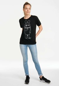 Schwarzes Baumwoll-T-Shirt mit einem weißen Cartoon-Maus-Print. Das Shirt hat kurze Ärmel und einen runden Halsausschnitt, kombiniert mit hellblauen Jeans.