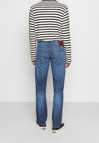 Jeans de denim azul con un corte recto, bolsillos traseros con un diseño de zigzag, combinados con una camiseta de rayas negra y blanca de manga larga.