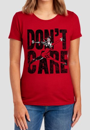 Red shirt with black text "DON'T CARE" and graphic of a woman in a jester costume leaping with arms outstretched.
