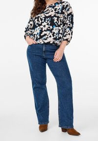 Blomstermønstret sort bluse med blå og beige blomster, parret med midt-blå lige ben jeans og brune hæl-støvler.