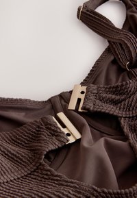 Haut de bikini marron à texture côtelée, avec fermoirs en métal doré et détails en tissu lisse. Bretelles réglables pour un meilleur ajustement.