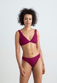 Bikini-set i en teksturert, mørkerød stoff. Har en trekantet bralette med brede stropper og matchende lavt skjørt bikini-bunn.