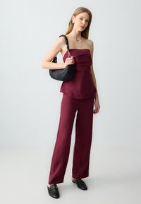 Bordeaux linnen strapless top gecombineerd met bijpassende wijde broek. Model heeft een zwarte leren schoudertas met een gevlochten band.