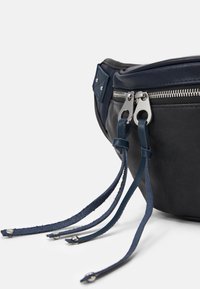 Svart läder midjeväska med marinblå detaljer, silverfärgad dragkedja och två dekorerande läderremmar med metallnitar. Rund formdesign.