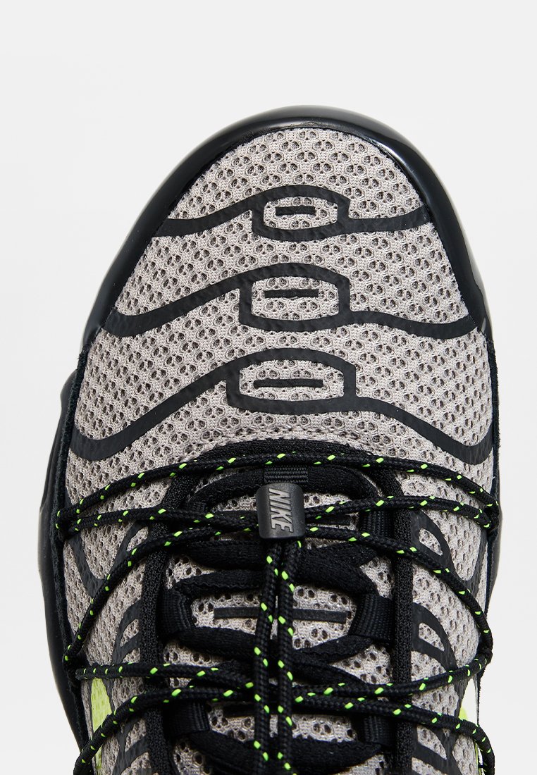 Scarpe da ginnastica Nike con una tomaia in rete grigia, accenti in gomma nera, lacci verdi e una suola texturizzata con motivi curvi distintivi.