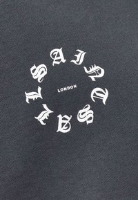 Czarna bawełniana koszulka z okrągłym białym nadrukiem ze stylizowanym napisem "SAINT" i "LONDON" na środku.