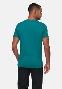 Teal t-shirt met korte mouwen van zachte stof, met een ronde hals en het woord "MAMMUT" in het wit gedrukt op de bovenrug.