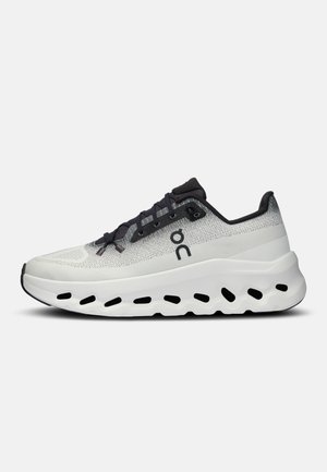 Světlé šedé a černé sportovní tenisky s prodyšným svrškem z meshu, černými tkaničkami a tlustou bílou podrážkou s černými vzorovanými výřezy.