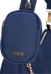 Sac à main en cuir bleu avec une surface texturée, des accents en doré, et une petite pochette zippée attachée à la sangle. Logo de la marque visible.