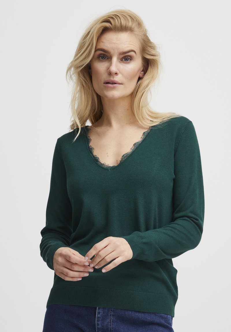 Grüner V-Ausschnitt-Pullover mit Spitzenbesatz, langen Ärmeln, gerippten Bündchen und Saum. Weiche Textur, figurnahes Design und minimalistischer Stil.