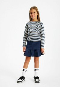 Randig långärmad skjorta i marinblått och krämfärgat, tillsammans med en marinblå volangkjol. Svartvita sneakers med randiga ankelsockor.