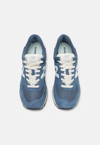 Kék velúr és hálós sportcipők fehér kiegészítőkkel és krém színű fűzőkkel, lekerekített orral és párnázott talppal. Látható New Balance márkázás.