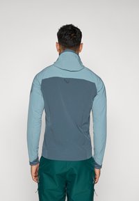 Két árnyalatú kék, testre szabott kabát magas gallérral, texturált anyagból, logóval a hátsó részen. Hosszú ujjakkal és letisztult dizájnnal rendelkezik.