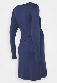 Mörkblå långärmad klänning med lätt puffade axlar och figursydd midja, visad bakifrån på en mannekäng.