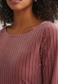 Tekstuuriga helesinine topp, millel on chevron muster, lai kaelus ja pehme kangas, mis voolab sujuvalt üle õlgade.