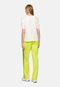 Weißes Baumwoll-T-Shirt mit kurzenÄrmeln, kombiniert mit leuchtend gelben Jogginghosen, die seitliche Streifen und eine strukturierte Oberfläche aufweisen.