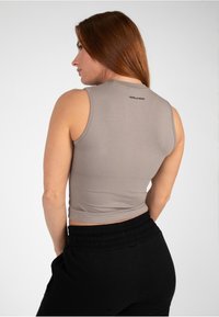Grijze mouwloze crop top met een aansluitend ontwerp. Het heeft een ronde halslijn en een klein logo op de rug, gecombineerd met zwarte relaxed-fit broek.