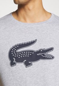 Camiseta de algodón gris con un gran gráfico de cocodrilo negro con patrones triangulares en su espalda. Diseño de cuello redondo con mangas cortas.