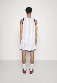 Maglia sportiva bianca e pantaloni corti con strisce verticali nere, con un bordo blu navy, abbinati a calze bianche e scarpe da ginnastica rosse.