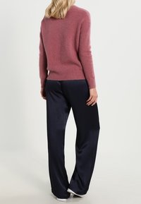 Maglione lavorato a maglia di colore rosa chiaro con una consistenza morbida e soffice, abbinato a pantaloni larghi in raso blu navy e scarpe bianche casual.
